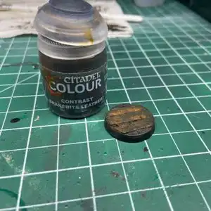 Muddy Warhammer base after being painted with Snakebite Leather brown, on top of a hobby cutting mat