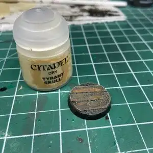 Muddy Warhammer base after being drybushed with Tyran Skull white, on top of a hobby cutting mat